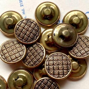 May include: A collection of antique brass buttons. Some buttons have a diamond pattern on the face, while others are plain. The buttons are in various sizes and show signs of age and wear.