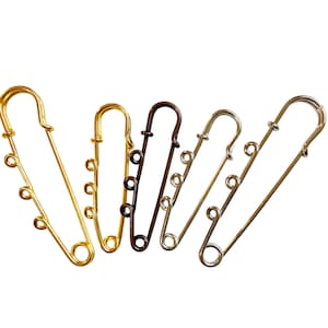 May include: Five metal safety pins in gold, bronze, and silver tones are arranged against a white background. Each pin has a looped head and a series of small loops along the pin's body, designed for attaching charms or beads.