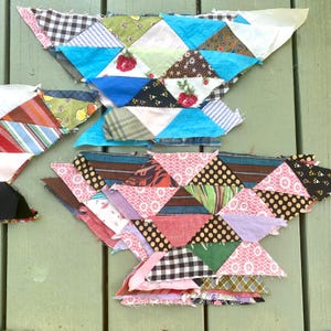 May include: Two unfinished quilt blocks made of patchwork fabric triangles. The top block is blue, green, and white. The bottom block is pink, brown, and green.