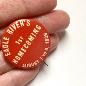 May include: A red button with white text that reads "Eagle River's 1st Homecoming August 1 to 8, 1929".