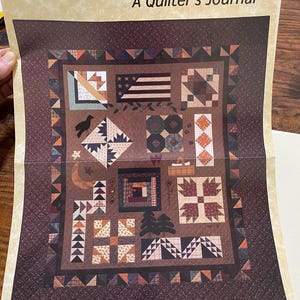 Könnte beinhalten: Ein braun-beiger Quilt mit verschiedenen geometrischen Mustern, darunter Sterne, Dreiecke und Quadrate. Der Quilt zeigt ein zentrales Design mit einem amerikanischen Flaggenmotiv und dem Text "Piecing the Trail to Kansas - A Quilter's Journal".