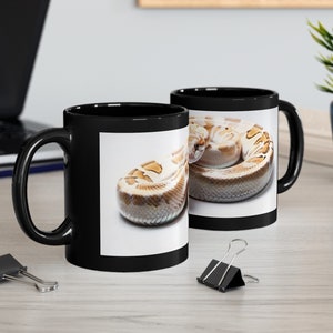 Könnte beinhalten: Zwei schwarze Kaffeetassen mit weißem Hintergrund und einem Bild einer zusammengerollten Schlange mit braunen und weißen Markierungen.