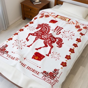 May include: White blanket with a red design featuring a horse, fireworks, and floral elements. The text "YEAR OF THE HORSE" and "2026" are also visible. The blanket is on a bed with a wooden frame.