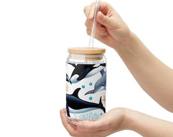 May include: A clear glass reusable water bottle with a bamboo lid and a straw. The bottle has a colorful design featuring orcas and dolphins swimming in the ocean.