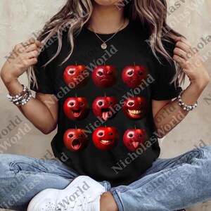 May include: Black t-shirt featuring a series of red apples with various facial expressions. The apples have different emotions, including happy, sad, and surprised. The shirt is a crew neck style.