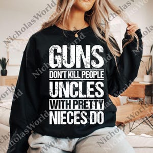 Puede incluir: Sudadera negra con texto blanco: "GUNS DON'T KILL PEOPLE UNCLES WITH PRETTY NIECES DO". La sudadera es de manga larga y cuello redondo.