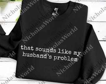 Könnte beinhalten: Schwarzes Sweatshirt mit dem weißen Text "that sounds like my husband's problem". Das Kleidungsstück ist ein Rundhals-Stil und wird auf einer weißen Holzoberfläche präsentiert.
