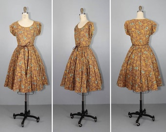 May include: A brown and yellow floral print dress with a brown belt. The dress has a full skirt and short sleeves. The dress is on a mannequin.