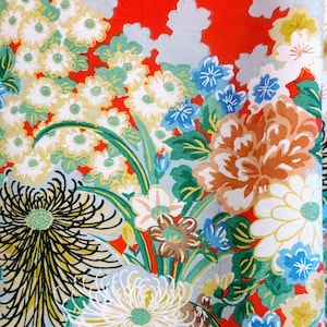 May include: A vibrant red fabric featuring a dense floral pattern with white, yellow, and blue chrysanthemums, green leaves, and light gray cloud-like shapes. The design includes large, detailed flower heads with thin petals and smaller blossoms.