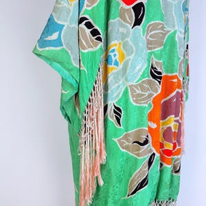 Puede incluir: Kimono floral verde con un vibrante estampado de flores rojas, azules y naranjas. El kimono presenta flecos melocot&oacute;n claro en el dobladillo y las mangas. La tela tiene un brillo sutil.