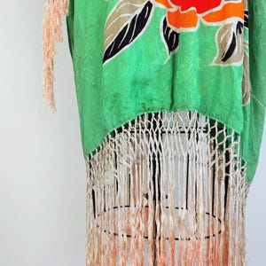 Puede incluir: Kimono de seda verde con un estampado floral en naranja, amarillo, marr&oacute;n y negro. El kimono tiene flecos color crema en la parte inferior con un efecto degradado, pasando de crema a melocot&oacute;n.