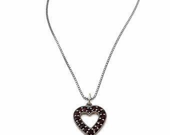 May include: A silver necklace featuring a heart-shaped pendant. The pendant is adorned with small, dark red gemstones, and the chain is a fine box chain. The heart has an open centre.