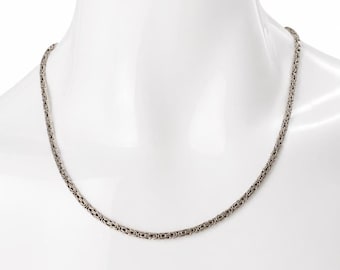 May include: A silver-colored chain necklace with a detailed, textured design. The necklace is displayed on a white mannequin, showcasing its intricate links and overall style. The chain is a classic accessory.