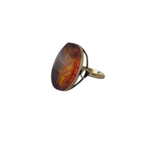 May include: A silver ring featuring a large, oval amber stone. The amber has a warm, translucent appearance with shades of brown and orange. The ring's band is a simple, classic design.