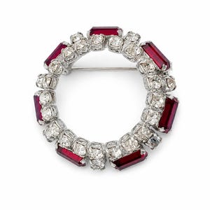 Peut inclure: Une broche circulaire dotée d'une monture en métal argenté ornée d'une alternance de cristaux blancs transparents et de pierres rectangulaires rouge foncé. Le motif est disposé en anneau continu avec une épingle visible au dos.