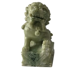 Può includere: Una scultura in giada verde di un cane foo cinese, una creatura mitica simile a un leone, seduto su una base quadrata.