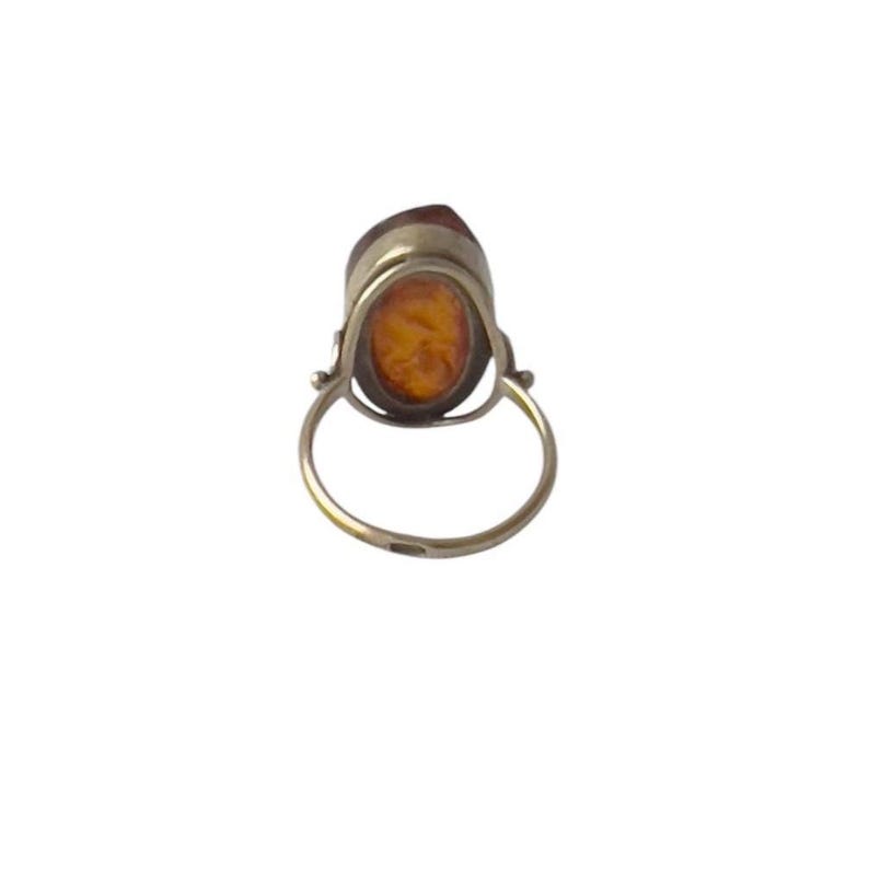 May include: A vintage ring featuring a large, oval amber stone set in a silver-toned metal. The amber has a warm, golden-orange hue. The ring's band is a simple, rounded design.