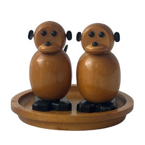 以下が含まれることがあります： サル型の木製塩コショウ入れ2個セット。塩コショウ入れは茶色で、目は黒く、口も黒いです。木製トレイに乗っています。