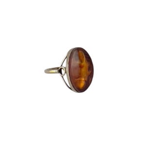 May include: Oval-shaped amber ring with a silver band. The amber stone has a warm, brown hue with lighter amber inclusions. The ring's design features a simple, elegant setting.