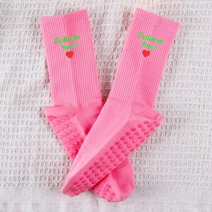 Op de afbeelding: Een paar roze sokken met gripdots op de onderkant. De sokken hebben de tekst "Follow Your" in groen met een klein rood hartje.