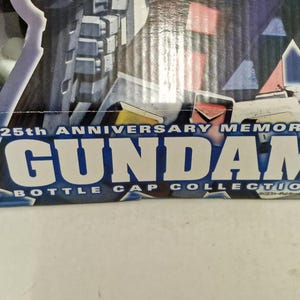 May include: Close-up of a box with the text "25th Anniversary Memorial Gundam Bottle Cap Collection" in white and blue. The box has a dark blue background with images of a Gundam robot.
