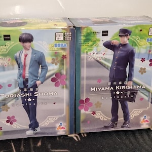 May include: Two SEGA anime figure boxes. One shows a figure in a blue blazer, red tie, and dark trousers, labelled "TORIASHI SHOMA." The other shows a figure in a dark blue uniform, labelled "MIYAMA KIRISHIMA." Both boxes have Japanese text and floral designs.