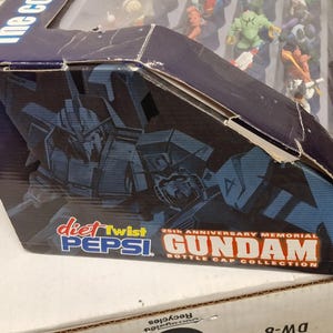 May include: A partially visible box for the 25th Anniversary Memorial Gundam Bottle Cap Collection. The box features a dark blue and black color scheme with images of Gundam robots and the Diet Twist Pepsi logo.