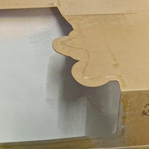 May include: Close-up of a partially open cardboard box. The box is a light brown color with a scalloped edge on the top flap. The interior of the box is white. The number "2" is handwritten on the side of the box.
