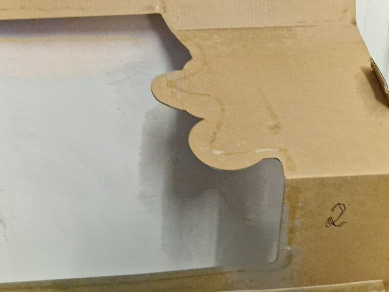 May include: Close-up of a partially open cardboard box. The box is a light brown color with a scalloped edge on the top flap. The interior of the box is white. The number "2" is handwritten on the side of the box.