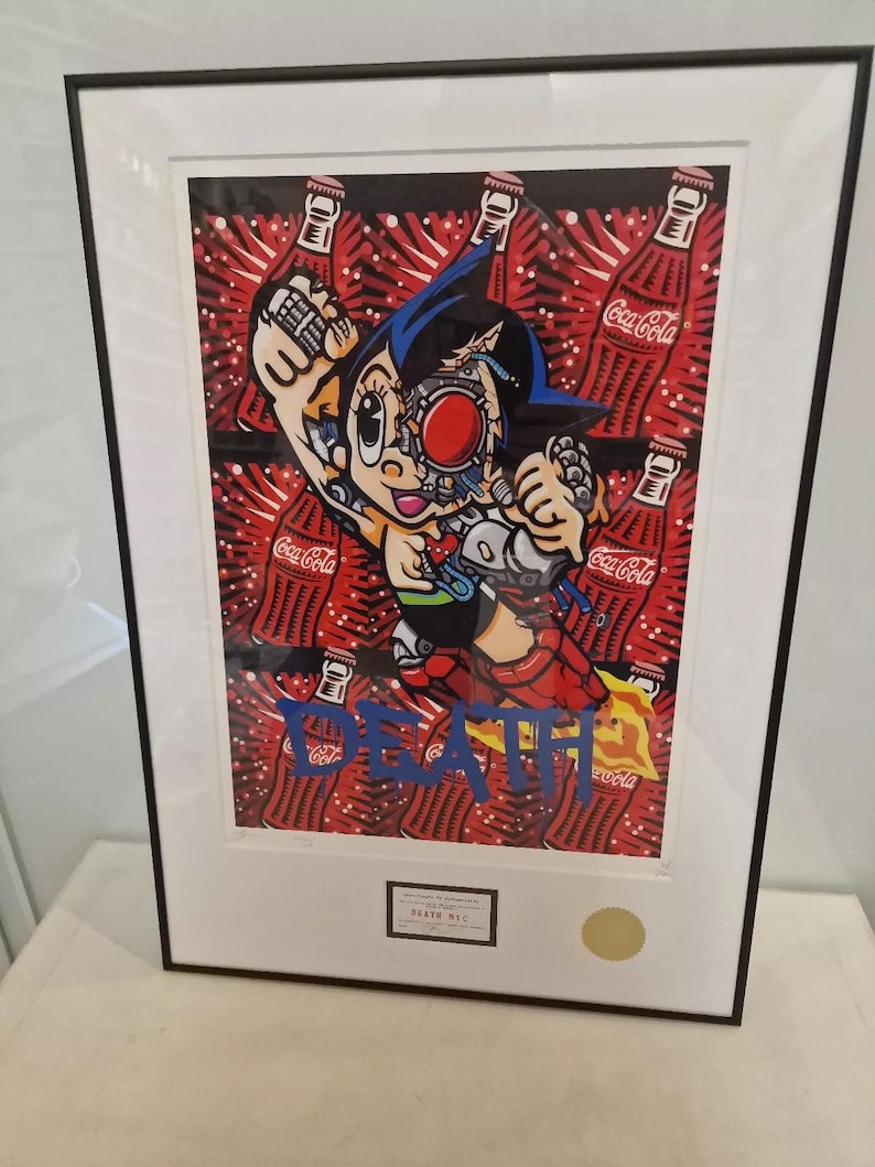 May include: A framed print of a cartoon character with a robotic head, surrounded by Coca-Cola bottles. The character is wearing a blue and red suit and has a blue cape. The print is signed "DEATH NYC".