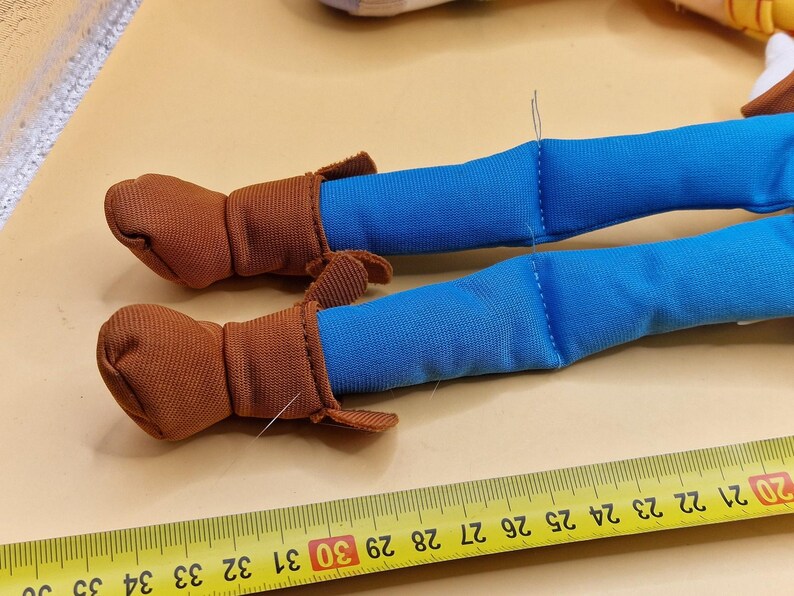 May include: Close-up of a toy doll's legs. The doll's legs are blue, with brown boots. A yellow ruler with black markings is in the foreground, measuring in inches.