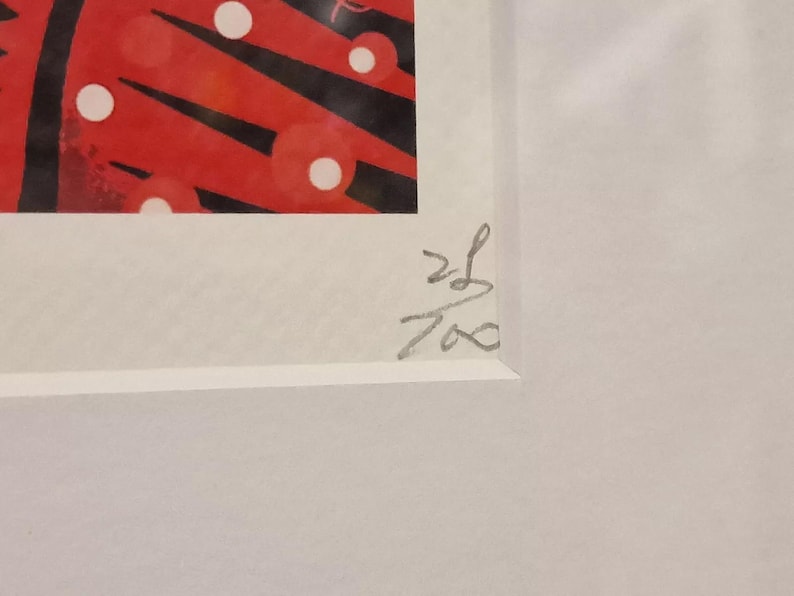 May include: A close-up of a white mat with a red and black abstract print. The print features white circles and black lines. The mat is signed in the bottom right corner with the number "26/700".