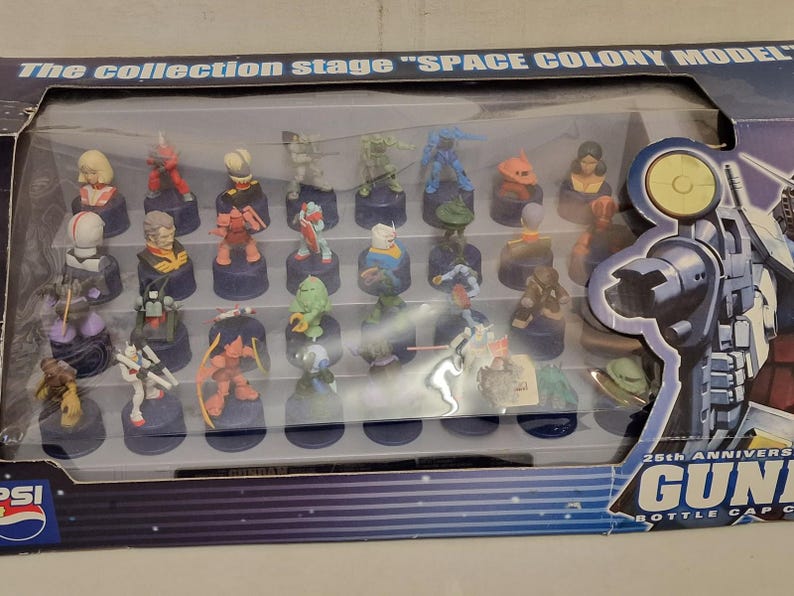 May include: A collection of colorful miniature figures displayed in a clear plastic case. The figures are on small, dark blue bases. The packaging reads "The collection stage SPACE COLONY MODEL" and "25th Anniversary GUNDAM Bottle Cap Collection".