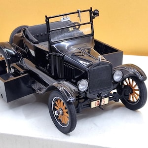 Può includere: Un modellino di auto nera in stile vintage con cassone, ruote a raggi in legno e una targa anteriore che riporta l'anno 1925. Il veicolo presenta una carrozzeria nera, interni neri e un cassone posteriore con la scritta R/S 033 impressa.