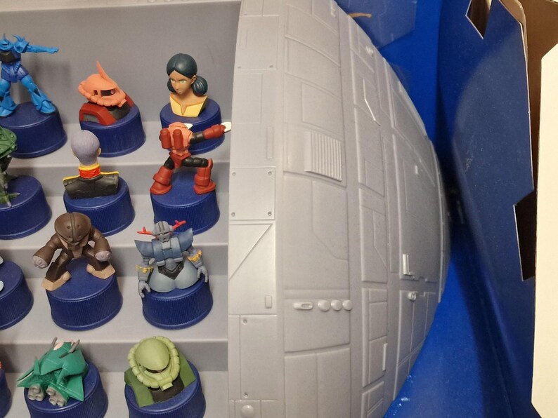 May include: A collection of colorful miniature figurines, each mounted on a blue cylindrical base. The figurines depict various characters, with details in red, orange, blue, and green. A large, gray, spherical structure is visible on the right side of the image.