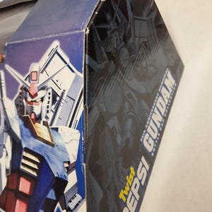 May include: A blue and white box featuring a Gundam robot illustration. The box has the text "COLONY MODEL" and "Twist Pepsi Gundam 25th Anniversary Memorial Bottle Cap Collection". The robot is primarily blue, red, and white.