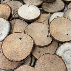 Może przedstawiać: Kolekcja małych, okrągłych drewnianych ozdób z naturalnym usłojeniem i krawędziami kory. Każda ozdoba ma mały otwór u góry i jest nawleczona na sznurek. Ozdoby mają różne kolory, od jasnobrązowego do średnio brązowego.