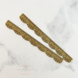 May include: Two decorative brass rulers with a scalloped edge and diamond cutouts. Each ruler is 12 inches long and features inch markings. The text "nana Company" is visible at the bottom.