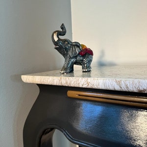 May include: A black painted side table with a white marble top. The table has a gold trim and a decorative elephant figurine on the top.