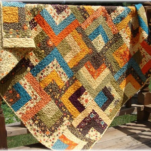 May include: A patchwork quilt with a variety of colors and patterns, including brown, orange, yellow, blue, and green. The quilt is made of squares and rectangles, and the seams are visible. The quilt is folded in half and is lying on a wooden surface.