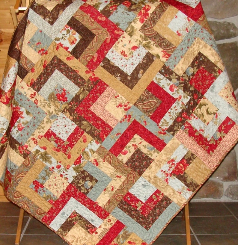 May include: A quilt with a patchwork design featuring various floral patterns in shades of red, brown, beige, and blue. The quilt is made with a variety of fabrics, including paisley and floral prints.