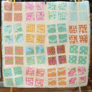 May include: A patchwork quilt with a grid pattern featuring various floral and geometric prints in shades of pink, blue, green, and orange.