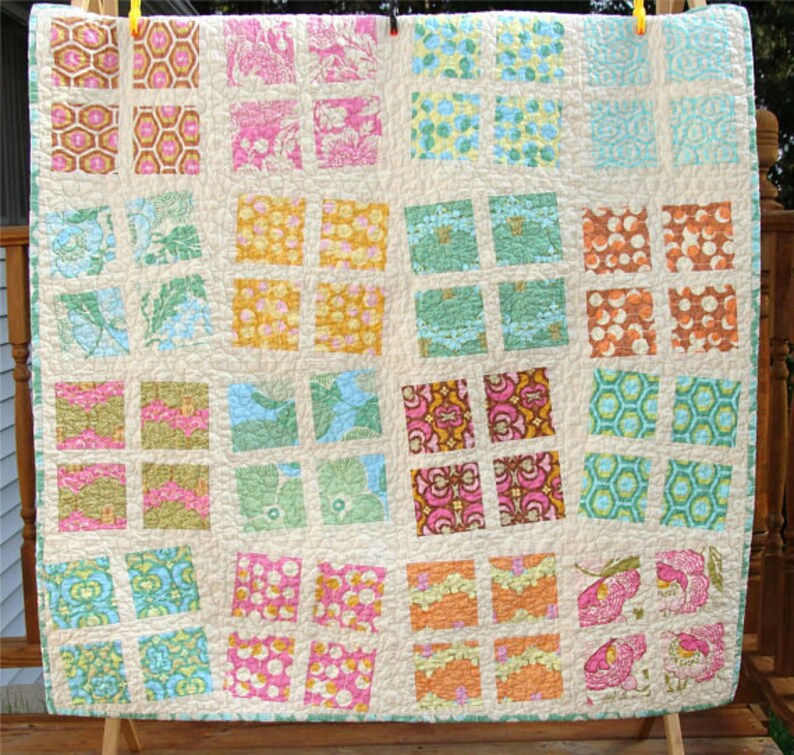 May include: A patchwork quilt with a grid pattern featuring various floral and geometric prints in shades of pink, blue, green, and orange.