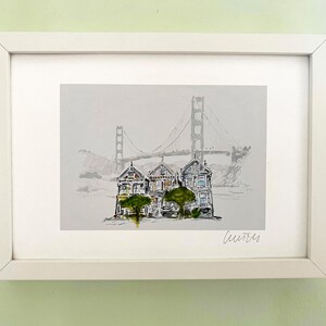 May include: A framed watercolour painting of three colourful Victorian houses with a green tree in front of them. The Golden Gate Bridge is in the background. The painting is signed "Leurrer".