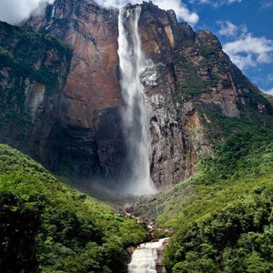 May include: A large waterfall tumbles down a sheer cliff face, surrounded by lush green vegetation. The waterfall is a natural wonder, with a powerful flow of water.