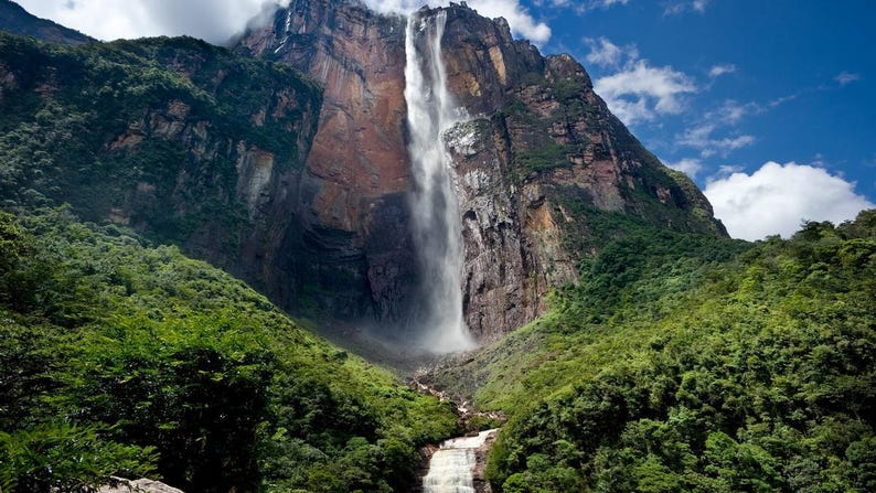 May include: A large waterfall tumbles down a sheer cliff face, surrounded by lush green vegetation. The waterfall is a natural wonder, with a powerful flow of water.