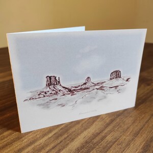May include: A watercolor painting of three red rock formations in a desert landscape. The sky is a light blue with a hint of pink. The painting is signed "Monica 2019".