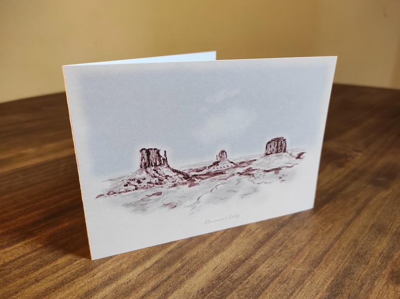 May include: A watercolor painting of three red rock formations in a desert landscape. The sky is a light blue with a hint of pink. The painting is signed "Monica 2019".