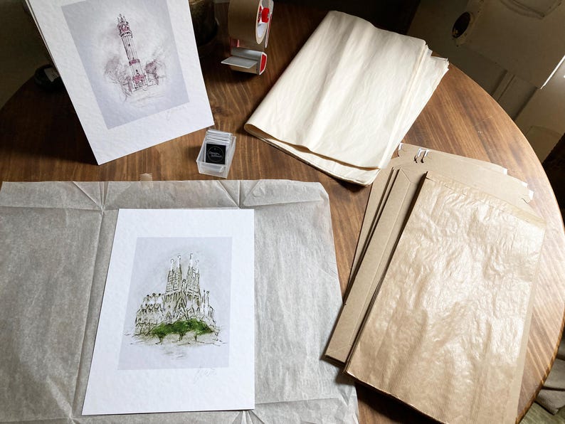 May include: A white mount with a black and white ink drawing of a building on top of it. The mount is on top of a brown paper bag. There is a roll of brown paper and a roll of white paper in the background.