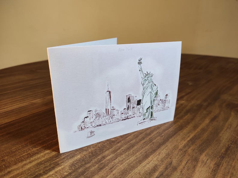 May include: A white card with a black and white illustration of the New York City skyline, including the Statue of Liberty and the Freedom Tower. The text "New York" is printed in the top right corner of the card.